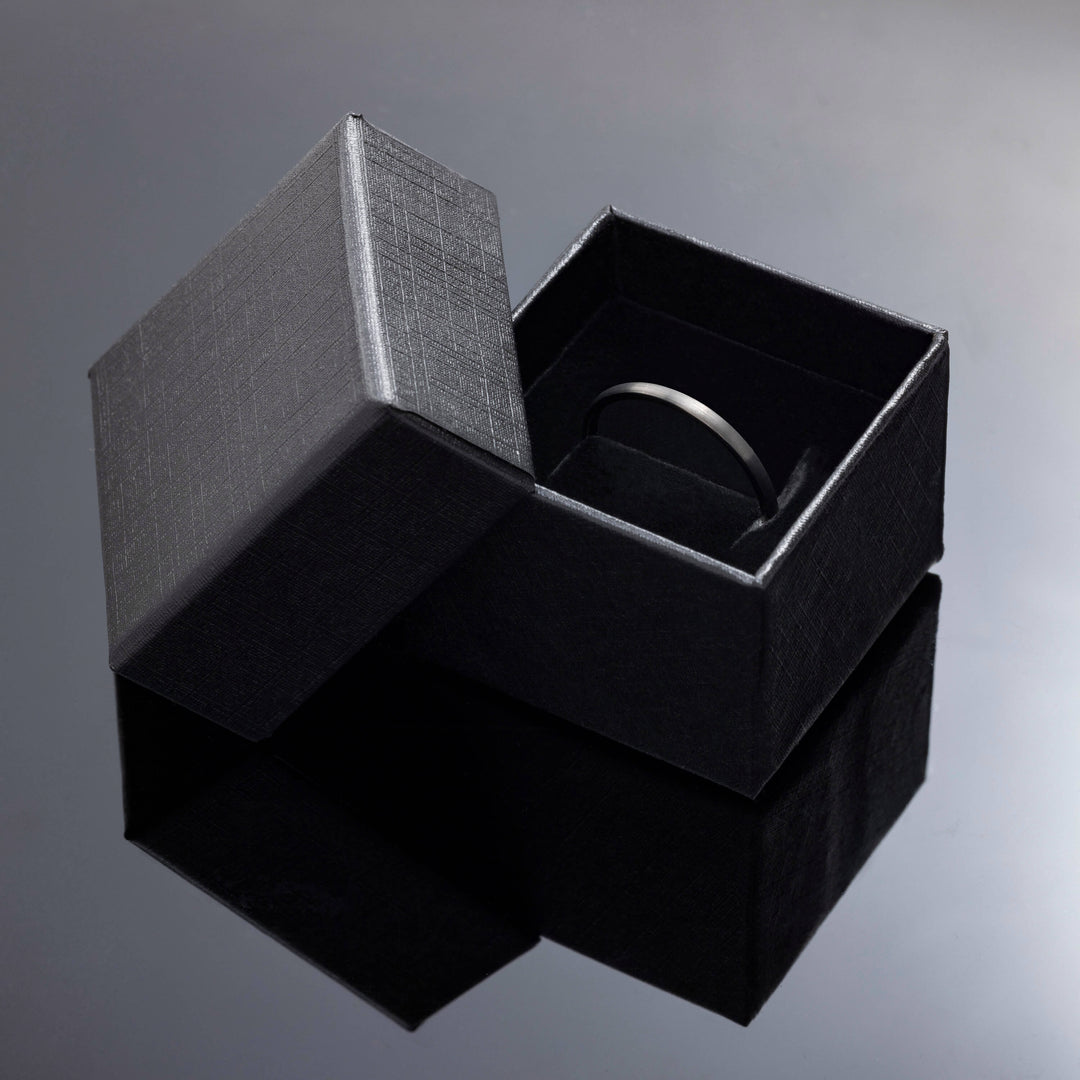 2mm thin gunmetal tungsten carbide wedding band in brushed style in black ring box, photo taken on black acrylic